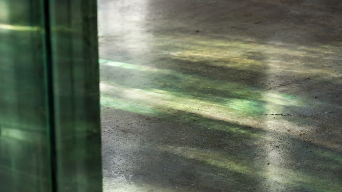 An abstract study: green glass reflections falling across worn concrete in soft window light